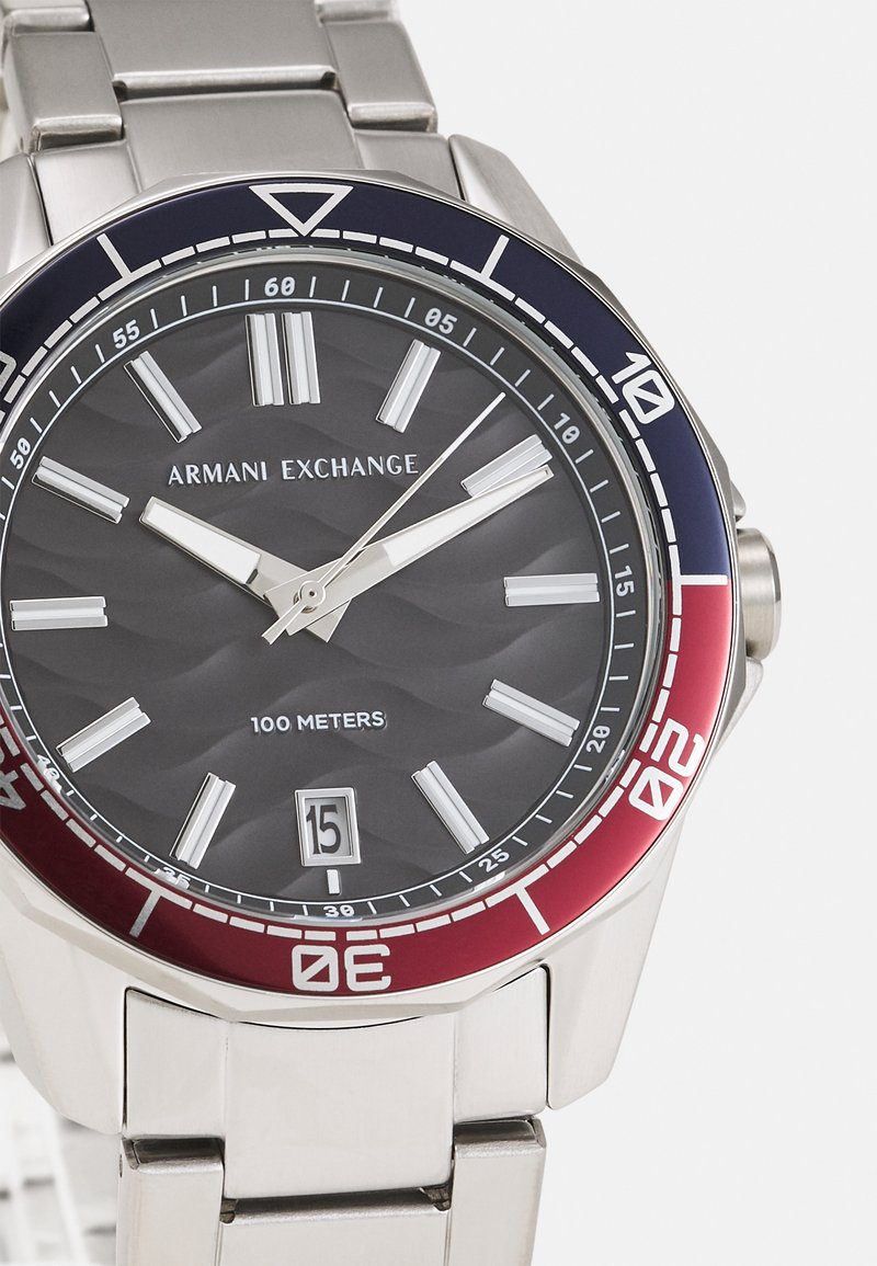 Orologio in acciaio inossidabile con quadrante nero testurizzato, indici delle ore argentati e una lunetta rossa e blu. Presenta una finestra della data alle 6.
