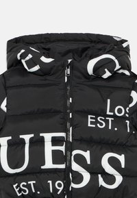 Doudoune noire avec capuche, dotée de textes et logos imprimés en blanc, fermeture éclair à l'avant et texture matelassée. Accents avec un logo triangulaire.