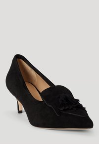 Fekete velúr magassarkú cipő hegyes orral, kis sarokkal, és díszes bojt részlettel az elején. Sima belső bélés és minimalista dizájn jellemzi.