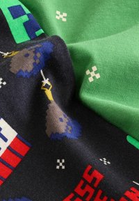 Black fabric with pixelated gaming characters, featuring colors like blue, yellow, and red, paired with a smooth green fabric piece.
