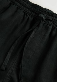 Black linen shorts with an elastic waistband, drawstring detail, and textured fabric. Features visible seams and pockets.