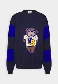 Pull en tricot bleu marine avec des manches rayées bleu et noir, présentant un motif d'ours portant un t-shirt blanc avec les lettres "VS" et "S" en jaune.