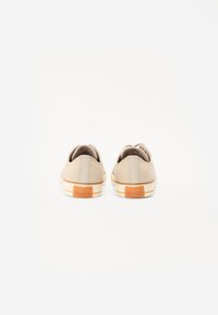 Baskets en toile beiges avec un design à profil bas, semelle en caoutchouc et logo All-Star orange au talon. Texture uniforme avec des accents beiges.