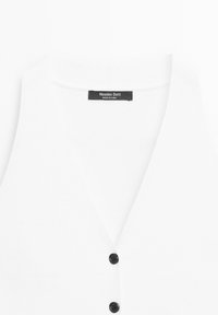 Bílý bezrukávový cardigan s výstřihem do V se dvěma černými knoflíky a štítkem "Massimo Dutti" na výstřihu.