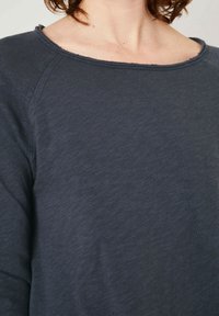 Tamsiai pilka ilgomis rankovėmis marškinėliai su plačia iškirpte ir suplėšytu kraštu. Pagaminta iš minkštos, tekstūruotos medžiagos su laisvu siluetu.