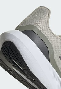 Svetlošedá športová obuv s textúrovaným vrchným materiálom, čierna gumová podrážka a biely akcent strednej podrážky. Obsahuje polstrovanú pätu a elegantné dizajnové prvky.