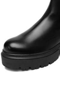 Czarny skórzany but z okrągłym noskiem i grubą, teksturowaną podeszwą z bieżnikiem, zaprojektowaną dla lepszej przyczepności i trwałości.