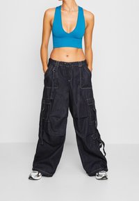 Blue ribbed crop top with a deep V-neck paired with loose black denim cargo pants featuring front pockets and drawstring waist.