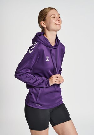Un hoodie violet avec une poche avant, une capuche à cordon et des accents argentés sur les manches. Matière extensible, associé à un short noir.