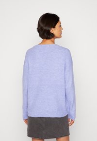 Pull en laine lavande clair avec texture côtelée, épaules tombantes et col rond, associé à une jupe en denim grise.