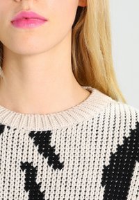 Pletený svetr s kulatým výstřihem; béžová základní barva s černými abstraktními vzory; texturovaná p�říze vytváří výrazný tkaný vzhled.