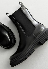 Czarne botki Chelsea z połyskującym lakierowanym wykończeniem, elastycznymi bocznymi panelami, pętlami do zakładania i grubymi teksturowanymi gumowymi podeszwami.