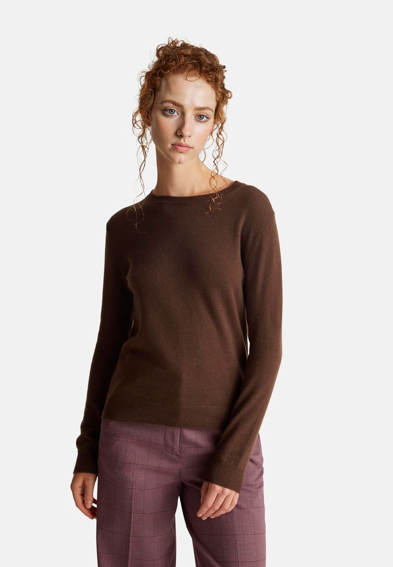 Brązowy sweter dzianinowy z okrągłym dekoltem i długimi rękawami, w zestawieniu z jasnofioletowymi, w kratę spodniami. Miękka tekstura, klasyczny krój.
