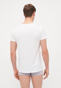 Weißes T-Shirt mit kurzen Ärmeln aus Baumwolle, mit Rundhalsausschnitt. Glatte Textur und lockere Passform, von hinten betrachtet.