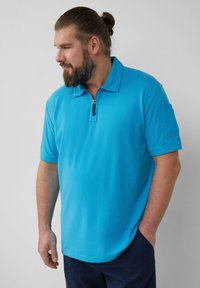 Turkusowa koszulka polo z zamkiem, krótkimi rękawami i teksturowanym materiałem. Posiada kieszonkę na lewym rękawie.