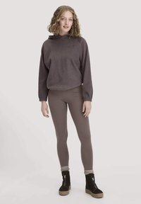 Paarse fleece hoodie met een trekkoord, gecombineerd met bruine leggings en zwarte enkellaarzen met een gestructureerde zool en gebreide accenten.