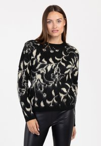 Schwarzer und cremefarbener Pullover mit floralem Muster, aus weichem Material, mit Rundhalsausschnitt und langen Ärmeln, kombiniert mit eleganten schwarzen Hosen.