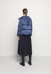 Granatowa kurtka puchowa z kapturem, z pikowanym wzorem i skróconym krojem. Nosi jej fason z długą czarną spódnicą oraz czarnymi botkami do kolan.