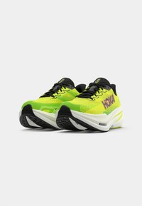 Baskets de course vert lime avec des accents noirs, dessus en maille texturée, semelle rembourrée et semelle extérieure à grip blanc et noir contrastant. Marque Hoka visible.