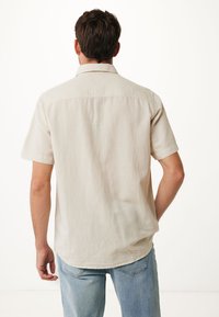 Camisa de manga corta de color beige, fabricada con un tejido ligero, con un corte recto y un cuello estándar. Textura suave, diseño casual.