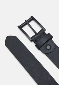 Ceinture en cuir noir avec une finition texturée, dotée d'une boucle en métal noir mat et d'un détail à pression près de la boucle. Trous pour l'ajustabilité.