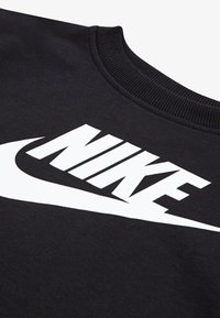 Μαύρη μπλούζα με στρογγυλή λαιμόκοψη, με μεγάλο λευκό λογότυπο "NIKE" και σχέδιο swoosh. Το ύφασμα έχει λεία υφή.