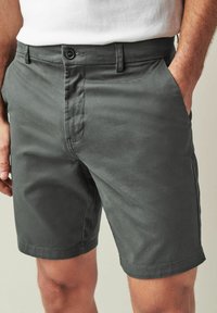 Șorturi gri din bumbac cu un front plat, două buzunare laterale, închidere cu nasture și o textură netedă. Lungime până la mijlocul coapsei, cu un tiv simplu.