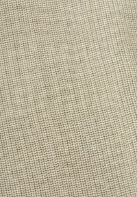 Gros plan d’un tissu beige tricoté avec une texture côtelée montrant des rangées verticales de mailles uniformes.