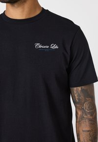 Schwarzes Baumwoll-T-Shirt mit kleinem weißen Logo "Closure Ldn" auf der linken Brust. Kurze Ärmel und klassischer Rundhalsausschnitt.