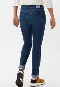 Mörkblå denimjeans med slim fit, medelhög midja och uppvikt fåll. Har bakfickor och en etikett på midjebandet.