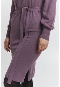 Abito a maglia in malva con maniche lunghe, cintura in vita, spacco laterale e texture a coste. L'abito ha una vestibilità comoda e un aspetto morbido.
