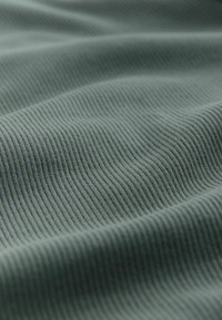 Textured fabric in a muted green color, featuring a ribbed pattern with fine ridges. Soft and flexible, displaying gentle folds and curves.