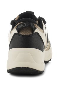 Zapatilla negra y marrón con talón de cuero negro texturizado, entresuela crema y un logotipo en la lengüeta del talón. El diseño es deportivo y funcional.