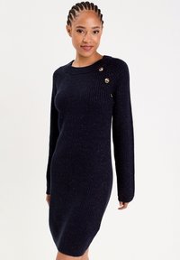 Dzianinowa sukienka w ciemnogranatowym kolorze z ryflowaną teksturą i długimi rękawami. Posiada trzy złote guziki na lewym ramieniu jako dodatkowy detal.