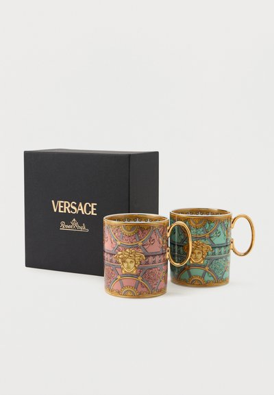 Δύο περίτεχνα φλιτζάνια καφέ Versace με χρυσές λαβές, ένα ροζ και ένα πράσινο, δίπλα σε ένα μαύρο κουτί με την επωνυμία Versace Rosenthal.