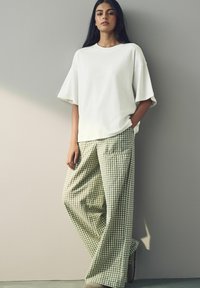 Bílé oversized tričko s krátkým rukávem v kombinaci se širokými kalhotami s zeleným kostkovaným vzorem. Jemná textura a uvolněný střih po celém obvodu.