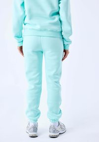 Sudadera de color verde menta y joggers a juego, hechos de un material suave. Los pantalones de chándal tienen puños elásticos y un diseño ajustado, combinados con zapatillas plateadas.