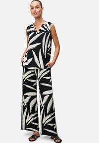 Top senza maniche a righe bianche e nere con scollatura a V, abbinato a pantaloni larghi con disegni di foglie coordinati. Indossato con sandali neri.
