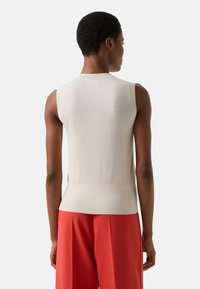 Hellbeiges �ärmelloses Oberteil mit gerippter Textur und tailliertem Schnitt, kombiniert mit knallroten Hosen mit weitem Bein. Glatter Stoff, minimalistisches Design.