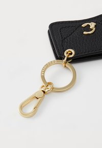 Porte-clés en cuir texturé noir avec quincaillerie dorée, doté d'un anneau circulaire et d'un clip à ressort pour attacher.