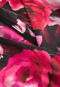 Květinová látka s velkými, živými růžovými růžemi na černém pozadí, se hladkou texturou a jemným leskem. Viditelné pozoruhodné detaily šití.