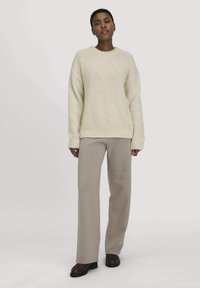 Crème kleurige chunky gebreide trui met een ronde hals en geribbelde zoom, gecombineerd met lichtbeige op maat gemaakte broeken en donkere instappers.