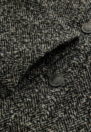 Textilie z vlněné směsi v texturovaném vzoru houndstooth, převážně černobílá, s detaily z tmavého kovového knoflíku.