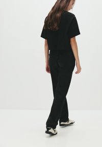 T-shirt noir coupé et jeans noirs. La tenue présente une coupe décontractée et un design minimaliste. Les chaussures sont des baskets blanches et noires.