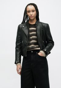 Czarna skórzana kurtka motocyklowa z prążkowaniem na ramionach, zestawiona z pasiastym swetrem i czarnymi jeansami z wysokim stanem.