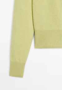Manica di un maglione verde chiaro con una texture morbida; presenta un polsino e un orlo a coste, mostrando un design semplice e pulito.