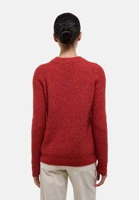 Pull en tricot rouge avec une finition texturée, manches raglan et col rond, vu de dos. Tissu doux et silhouette ajustée.