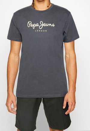 Osoba nosząca ciemnoszarą koszulkę z okrągłym dekoltem z białym logo "Pepe Jeans London", połączoną z czarnymi szortami, stojąca na jednolitym tle.