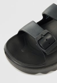 Black sandal with two wide straps and a buckled closure. Made of textured rubber, featuring a contoured footbed and a durable outsole.
