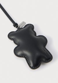 Fekete bőrből készült, mackó alakú kulcstartó varrással díszítve és levehető szíjjal. Fém címke márkajelzéssel rögzítve.